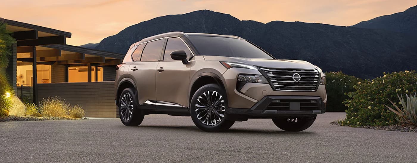 A tan 2024 Nissan Rogue is parked in a driveway after visiting a Nissan dealer.