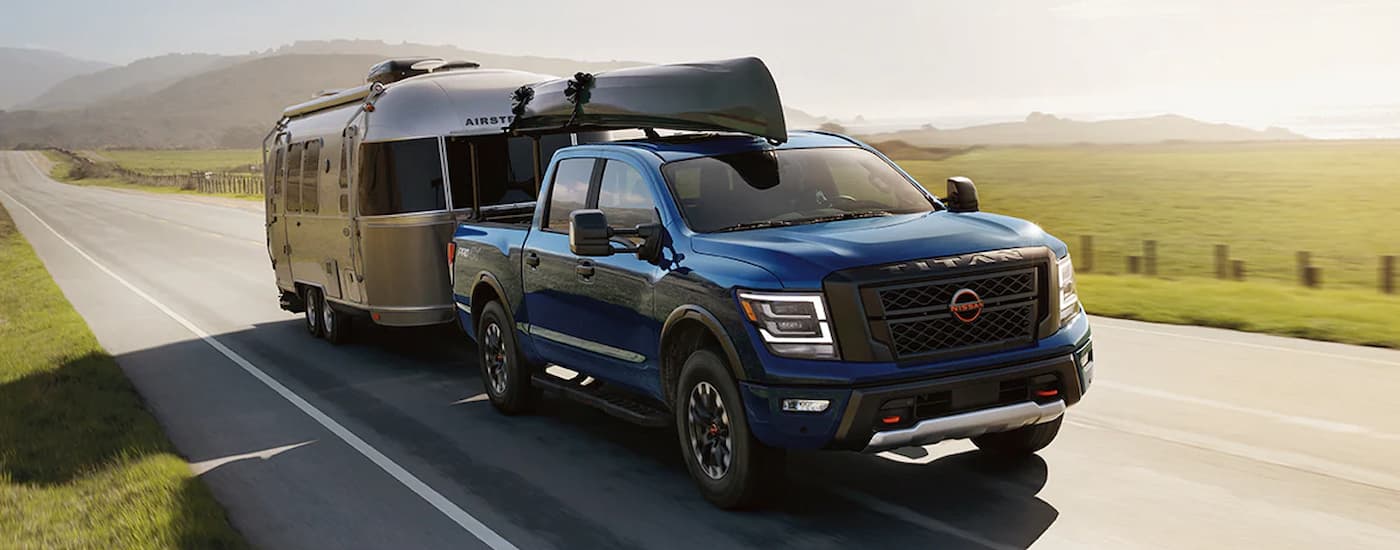 A blue 2024 Nissan Titan Crew Cab towing a camper trailer on an open road.