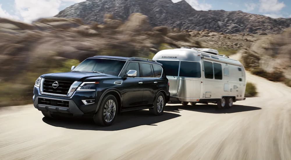 A dark blue 2024 Nissan Armada Platinum is towing a camper.