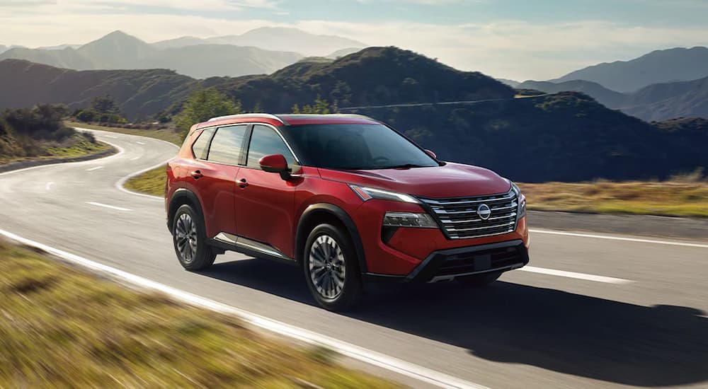 A red 2024 Nissan Rogue is driving on a mountain highway.