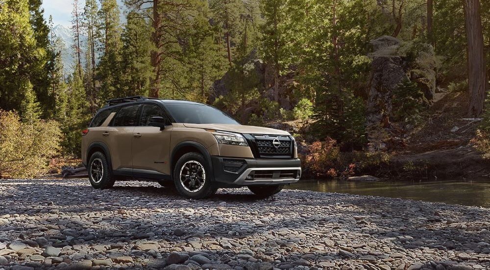 A tan 2023 Nissan Pathfinder Rock Creek parked off-road next to a stream.